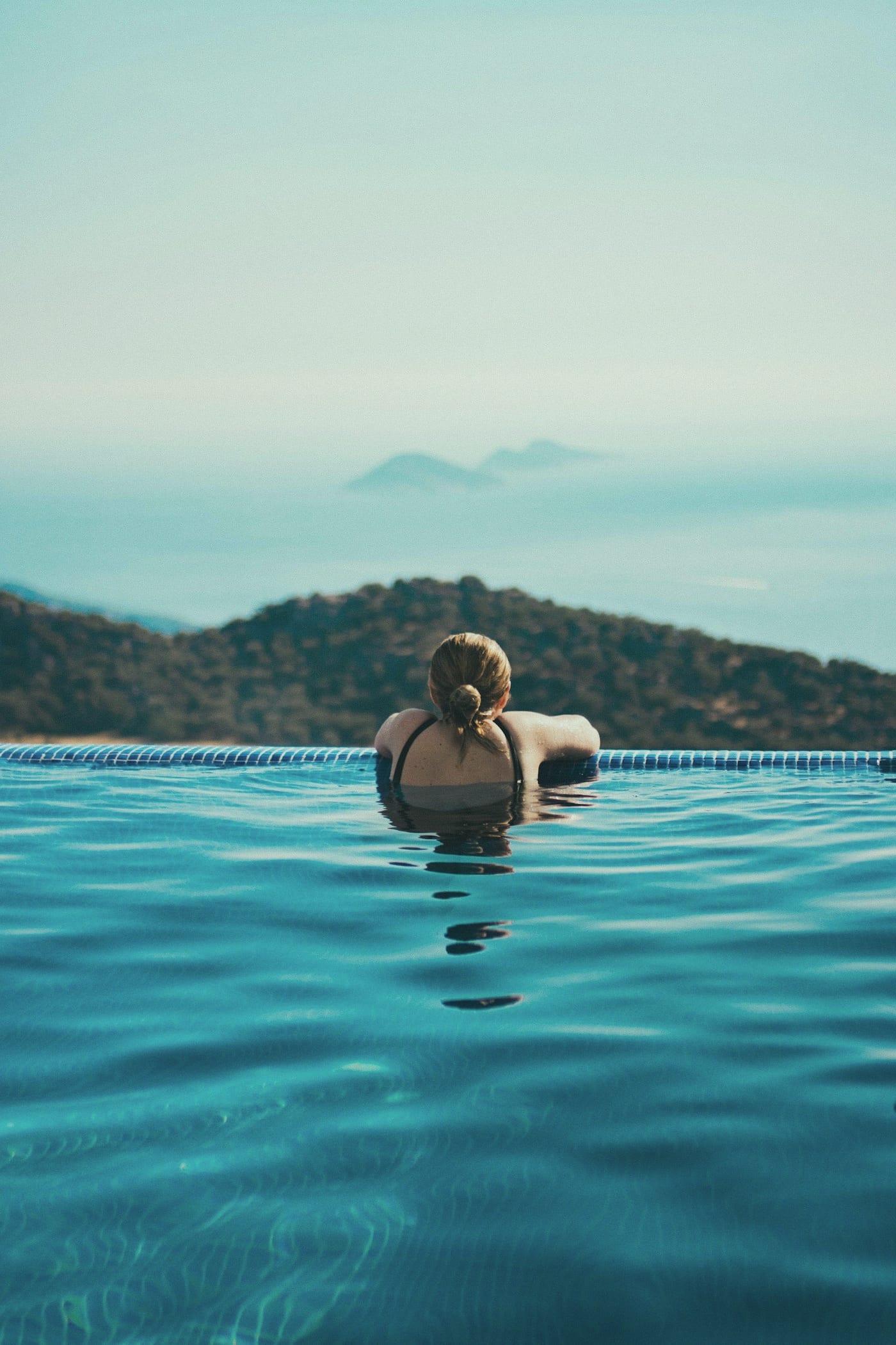 A lone figure at the far edge of an infinity pool, looking out to a pale Mediterranean sea.