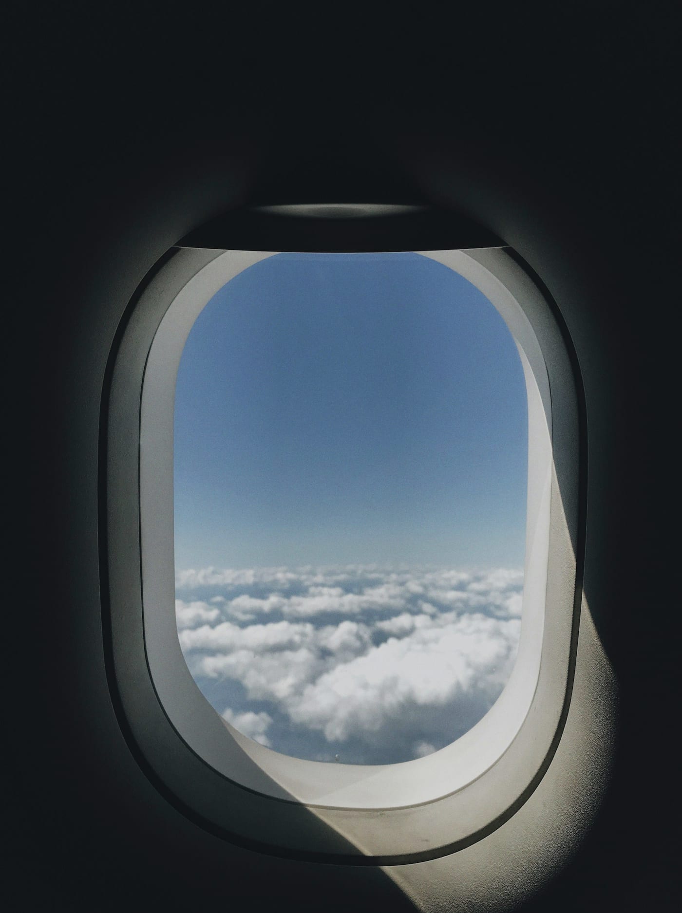 The view from an aircraft window over an unbroken bank of cloud, the cabin dark around it.